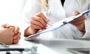 Lekarz rodzinny pisze skierowanie na rezonans. Pacjent czeka na diagnozę.