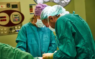 Chirurdzy w zielonych fartuchach wykonują artroskopię barku. W tle widać aparaturę medyczną.