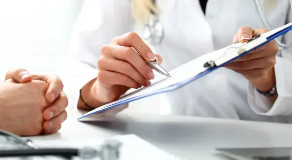 Lekarz rodzinny pisze skierowanie na rezonans. Pacjent czeka na diagnozę.