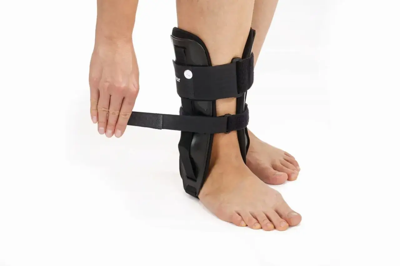 Dłoń zapina czarną ortezę na staw skokowy, zapewniając stabilizację i wsparcie podczas rehabilitacji.