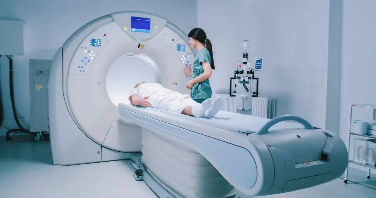 Pacjent leży na łóżku rezonansu magnetycznego, pielęgniarka przygotowuje badanie. Jak przetrwać rezonans magnetyczny? Spokój i zaufanie do personelu to klucz.