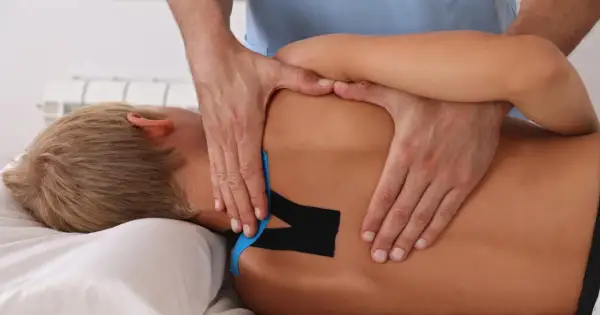 Fizjoterapeuta aplikuje taśmy kinezjotaping na plecy pacjenta.