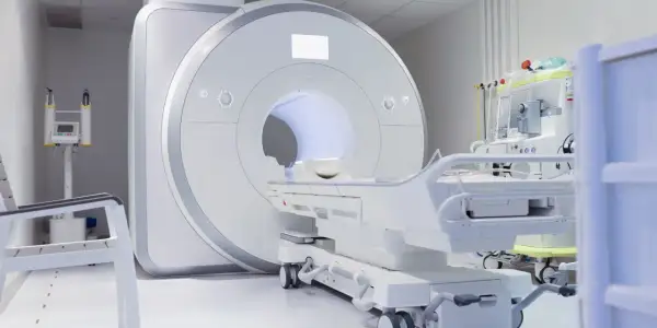 Nowoczesny gabinet diagnostyczny z aparaturą do rezonansu kręgosłupa szyjnego. Obok leżanka i sprzęt medyczny.