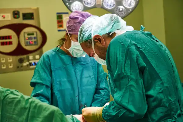 Chirurdzy w zielonych fartuchach wykonują artroskopię barku. W tle widać aparaturę medyczną.